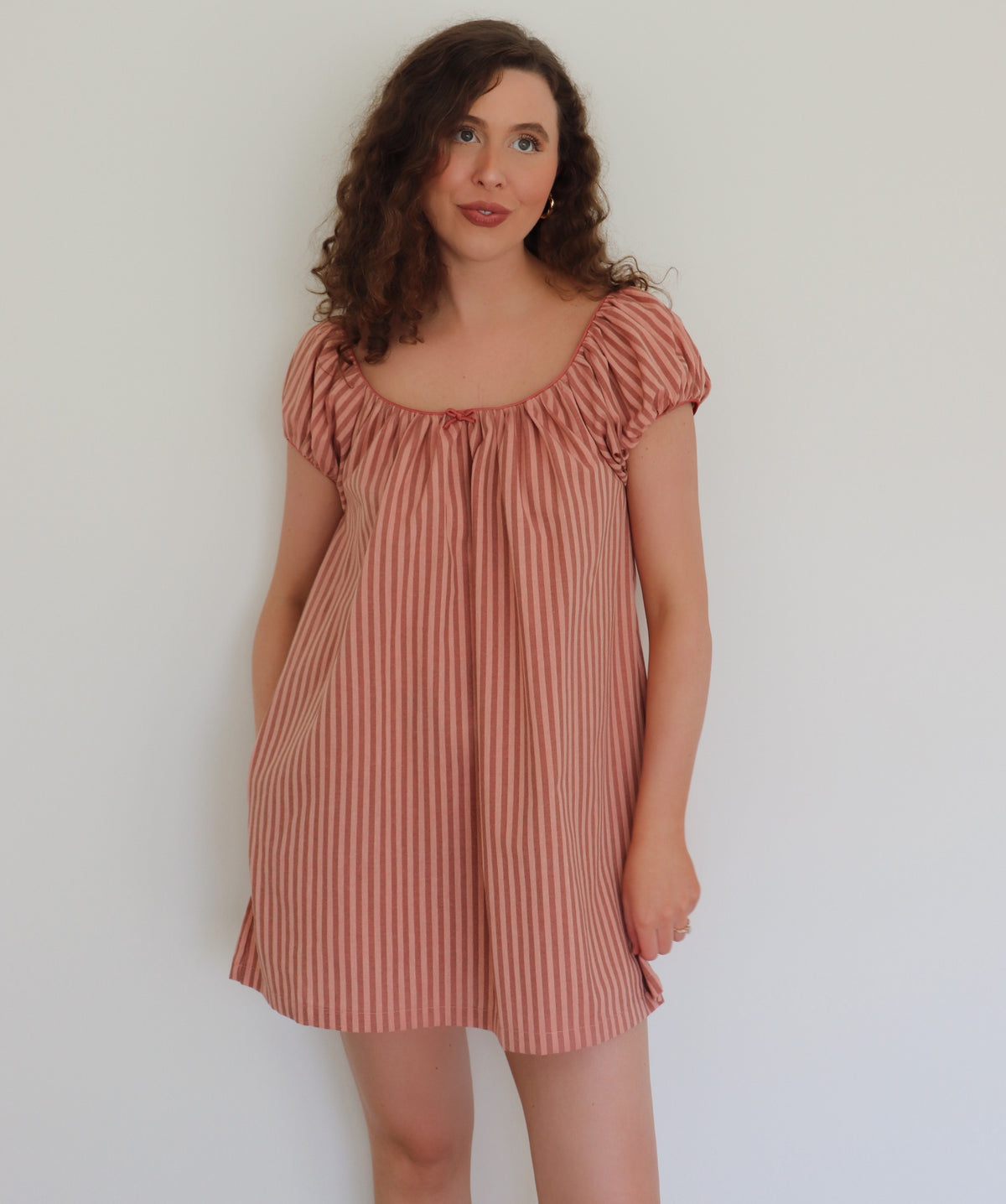 Woman wearing a peach striped dress against a plain background