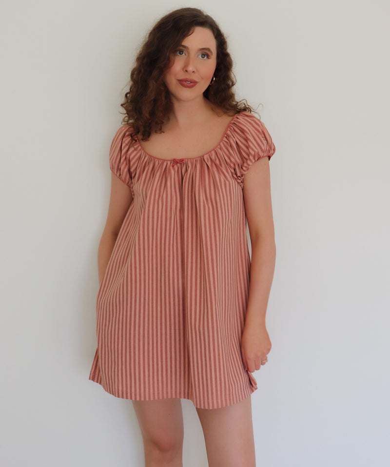 Woman wearing a peach striped dress against a plain background