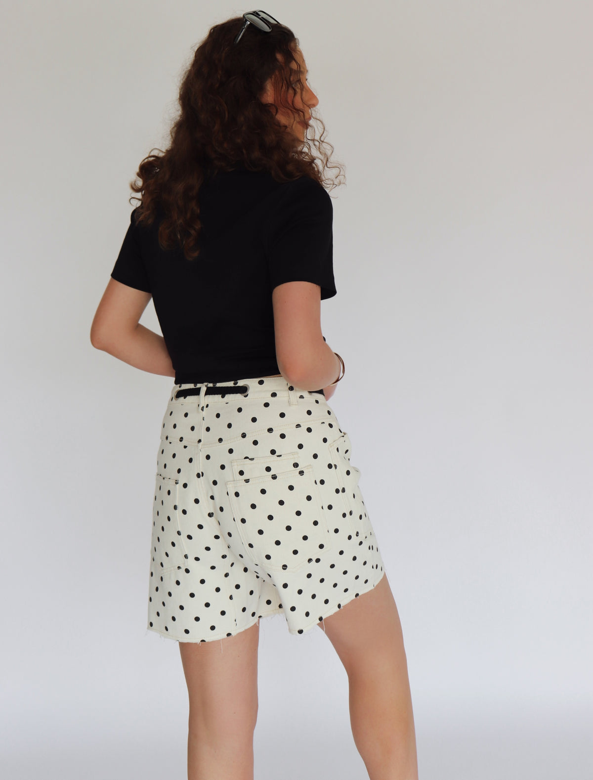 Woman wearing a black crop top and polka dot shorts against a plain background