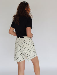 Woman wearing a black crop top and polka dot shorts against a plain background