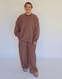 Woman wearing a brown and pink striped loungewear set in front of an off white wall.