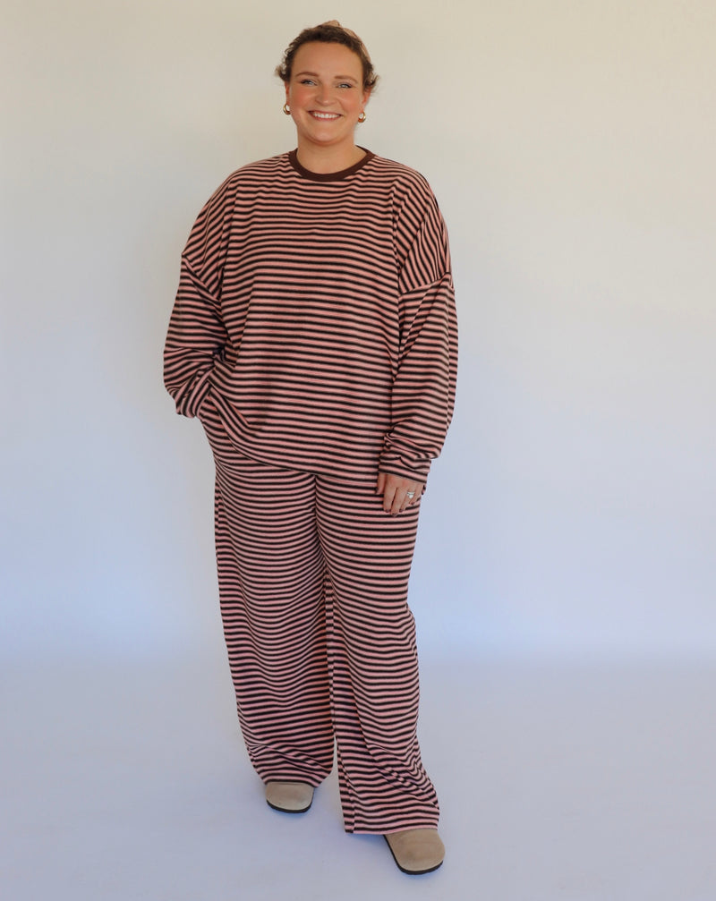 Woman wearing a brown and pink striped loungewear set in front of an off white wall.