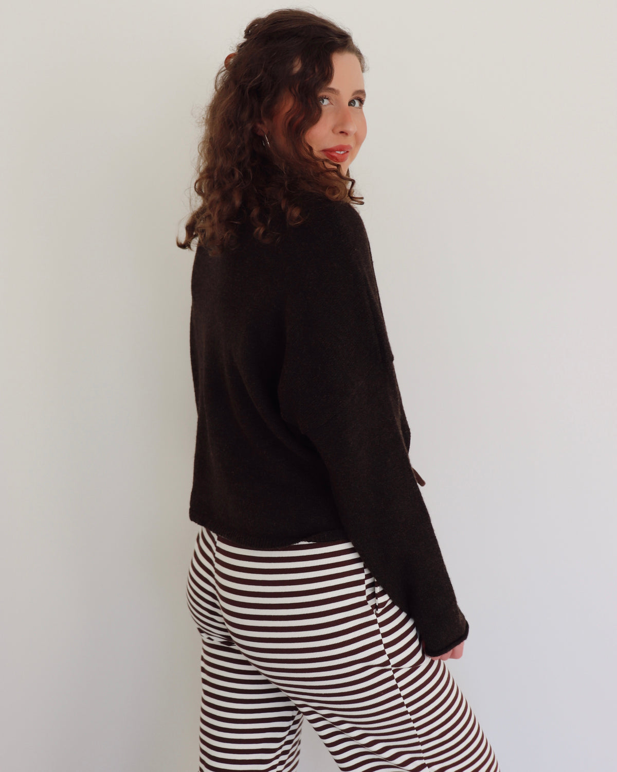 Woman wearing a chocolate brown cardigan and striped pants against a white background