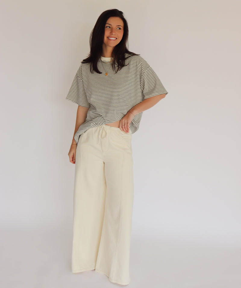 Woman wearing a striped shirt and cream wide-leg pants against a plain background