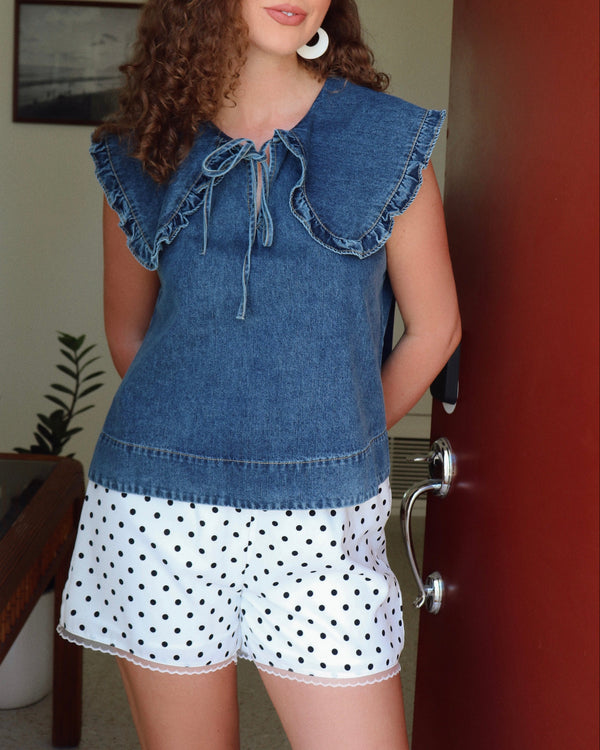 Woman wearing a denim top and polka dot shorts indoors.
