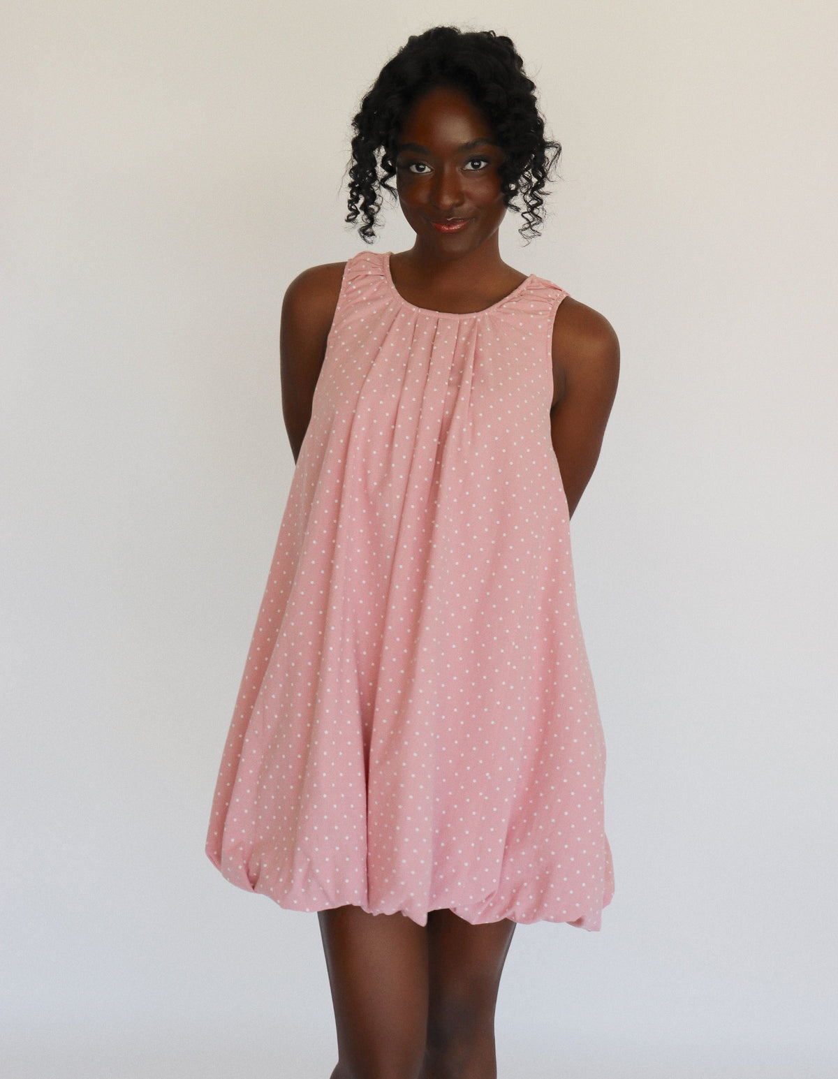Woman wearing a pink dress with white polka dots on it against a white background