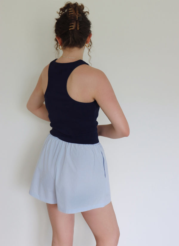 Person wearing a navy tank top and light blue shorts against a white wall