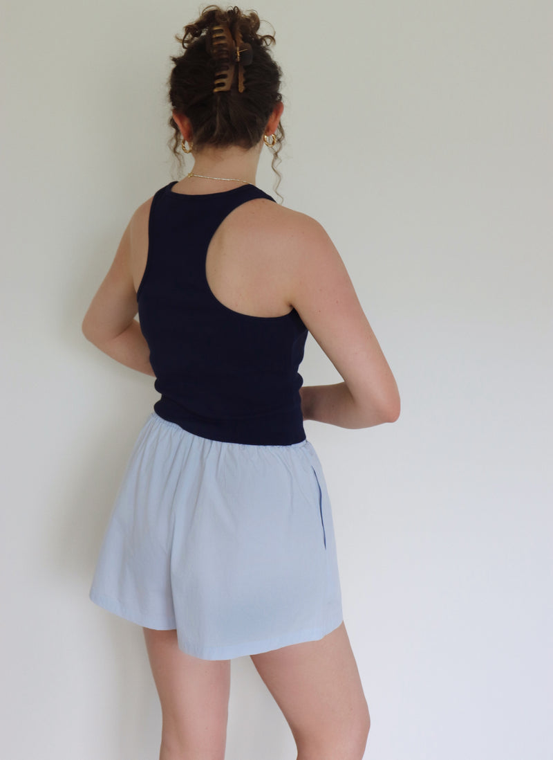 Person wearing a navy tank top and light blue shorts against a white wall