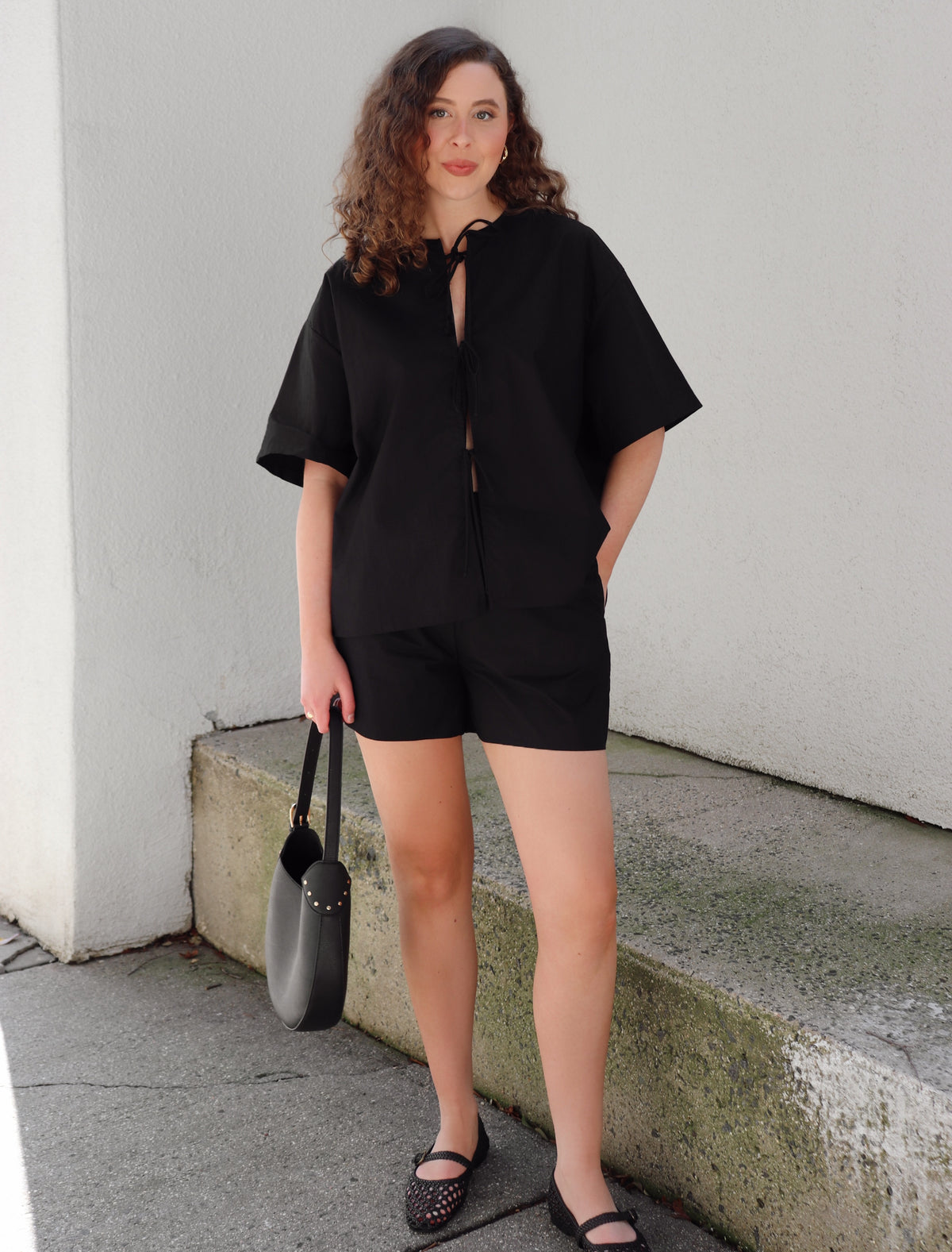 Woman in a black outfit standing on concrete background against a beige  wall.