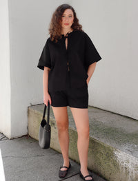 Woman in a black outfit standing on concrete background against a beige  wall.
