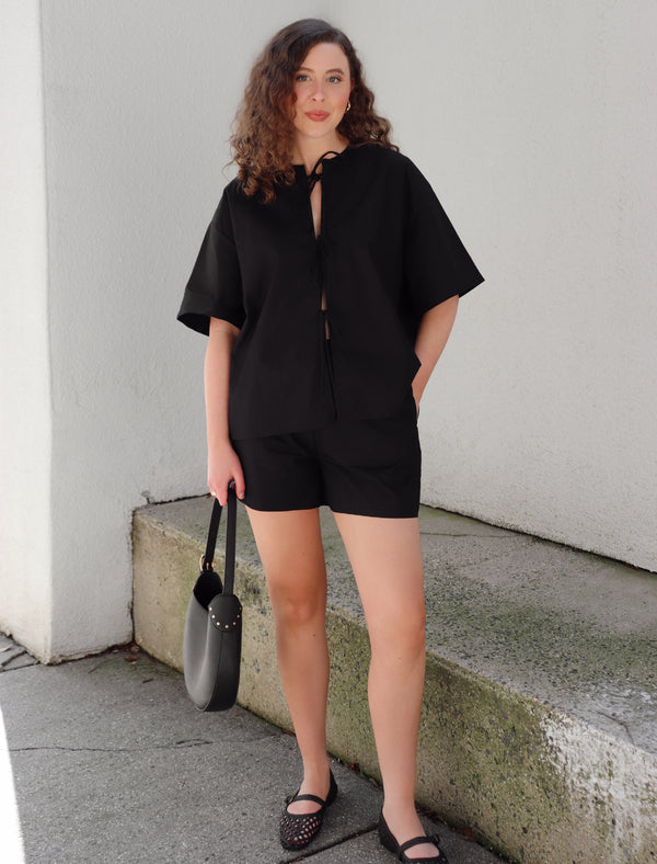Woman in a black outfit standing on concrete background against a beige  wall.