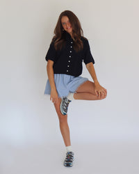 Woman wearing a navy short sleeve cardigan and light blue shorts against a white background