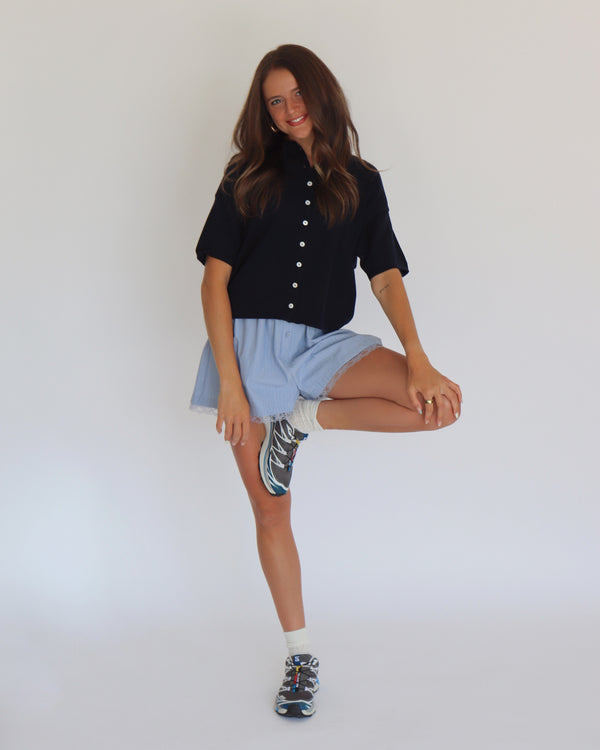 Woman wearing a navy short sleeve cardigan and light blue shorts against a white background