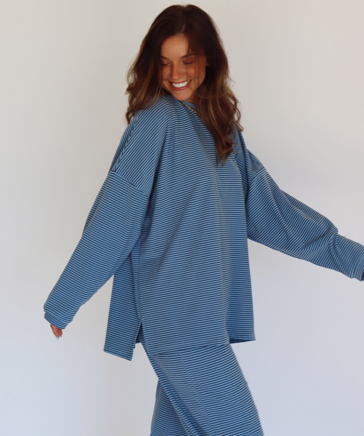 A woman modeling a matching blue striped lounge set, consisting of a long-sleeve top and wide-leg pants, against a plain white studio background.