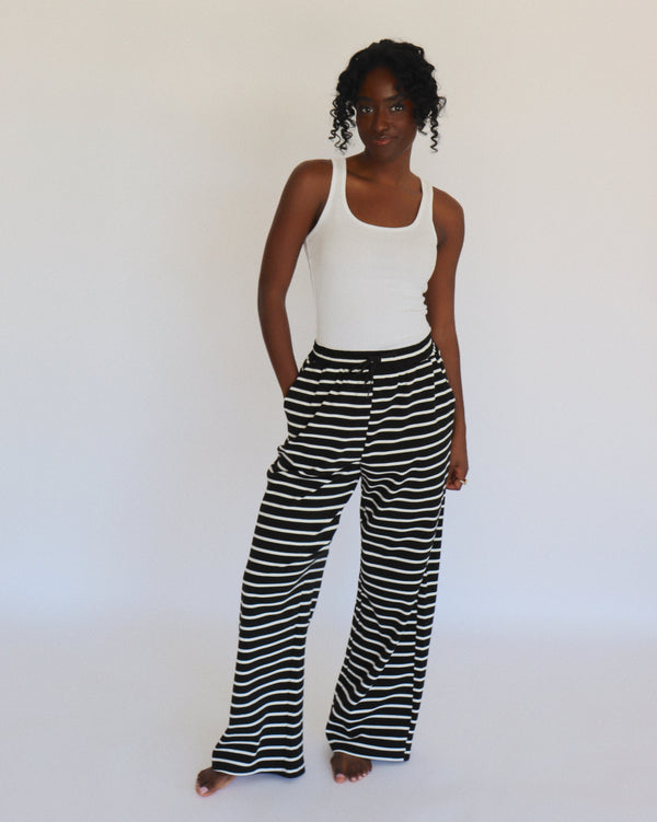 Woman wearing a white tank top and black and white striped pants on a white background