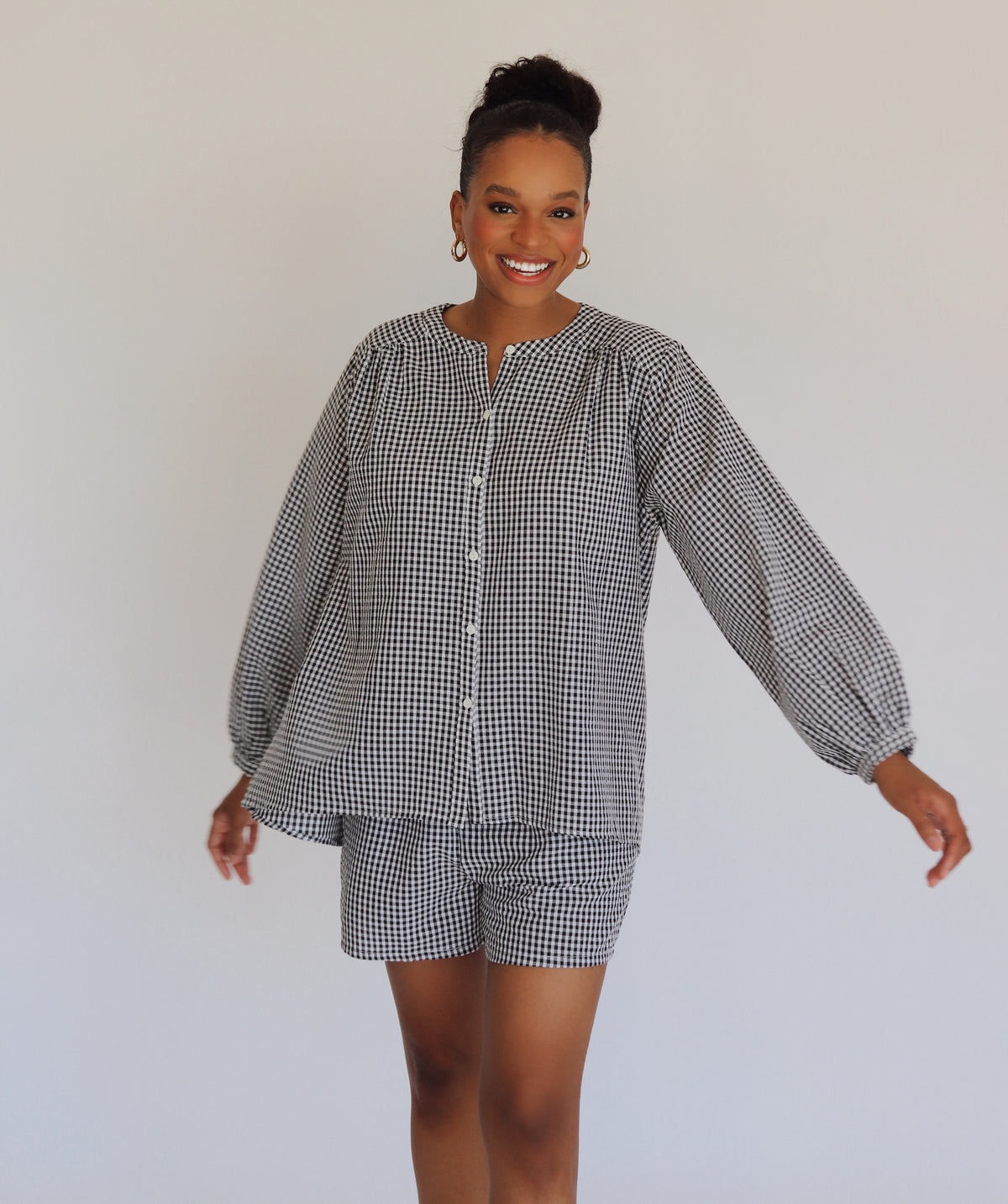 Woman wearing a checkered outfit with a long-sleeve top and shorts on a white background