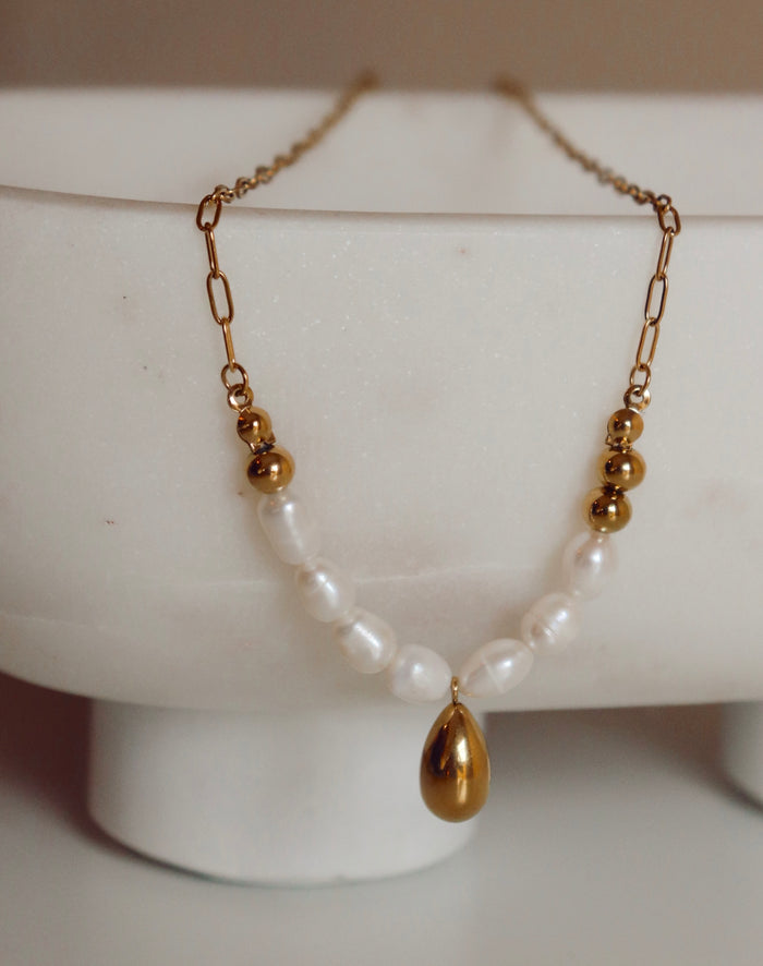 Necklace with gold teardrop pendant and pearl style chain on a white stand