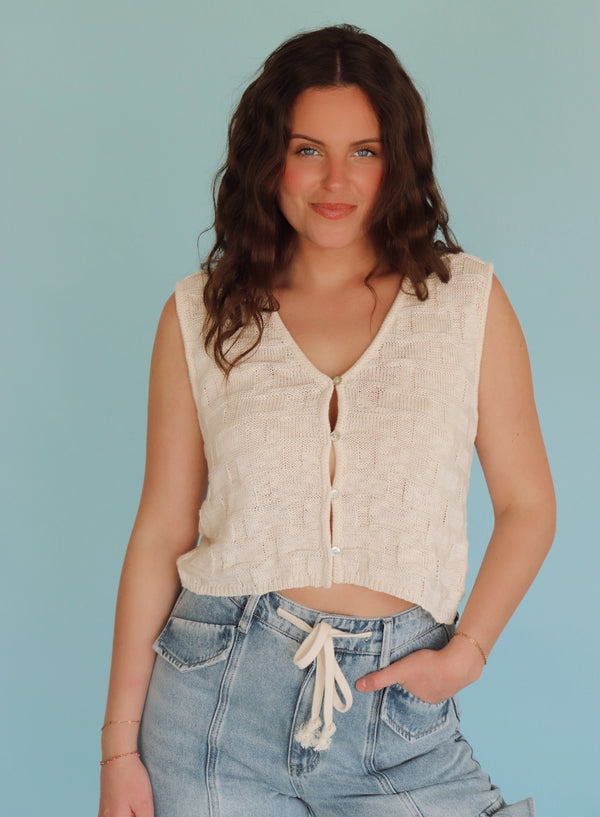 Woman wearing a cream vest and blue jeans against a light blue background