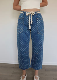 woman wearing white tank top and blue jeans with white polka dots on them against a white wall