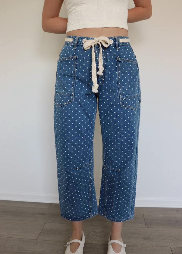 woman wearing white tank top and blue jeans with white polka dots on them against a white wall