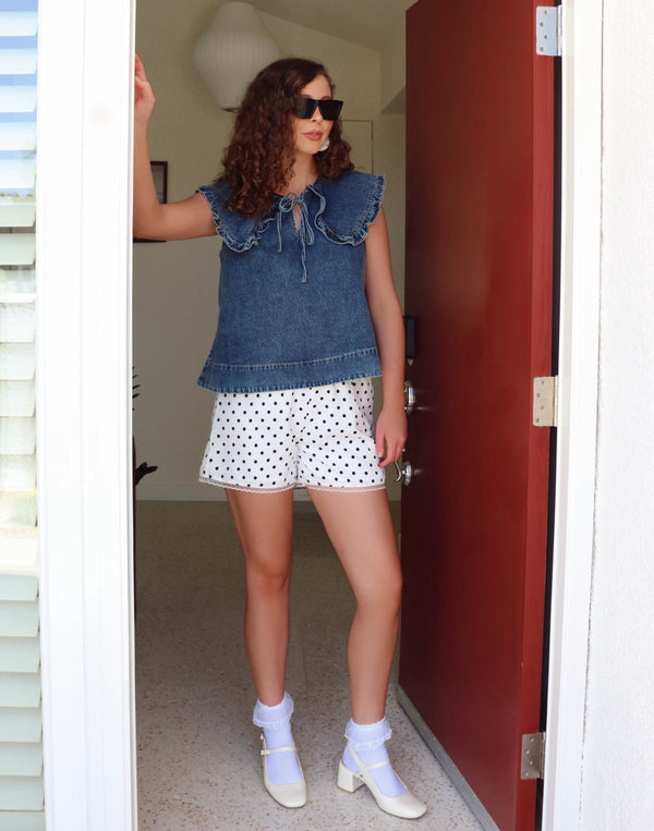 Woman wearing a denim top and polka dot shorts standing in a doorway.