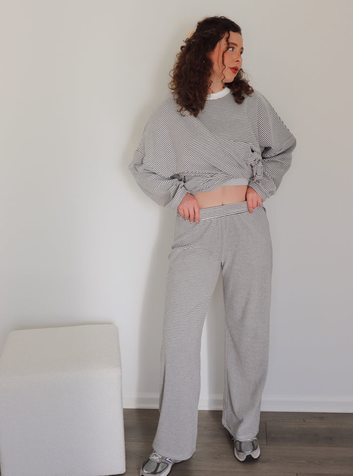 Woman wearing a gray striped outfit standing against a white wall.