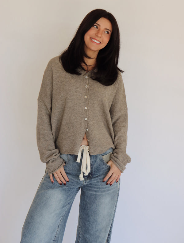 Woman wearing a taupe cardigan and blue jeans against a plain background