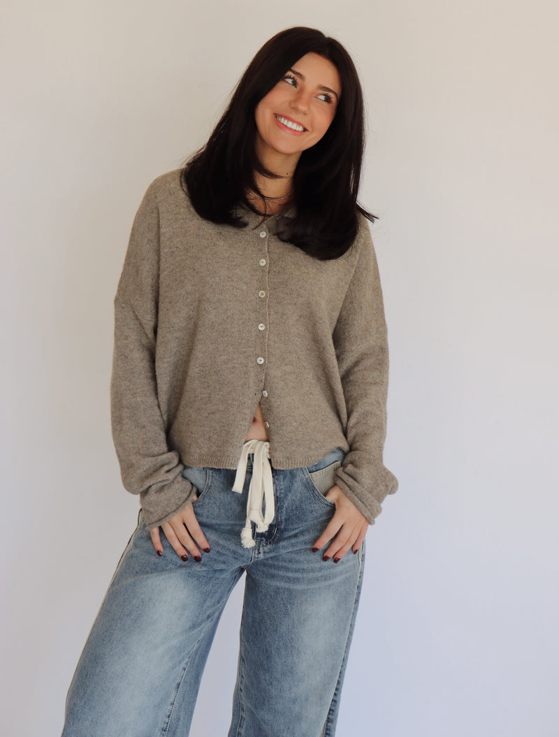 Woman wearing a taupe cardigan and blue jeans against a plain background