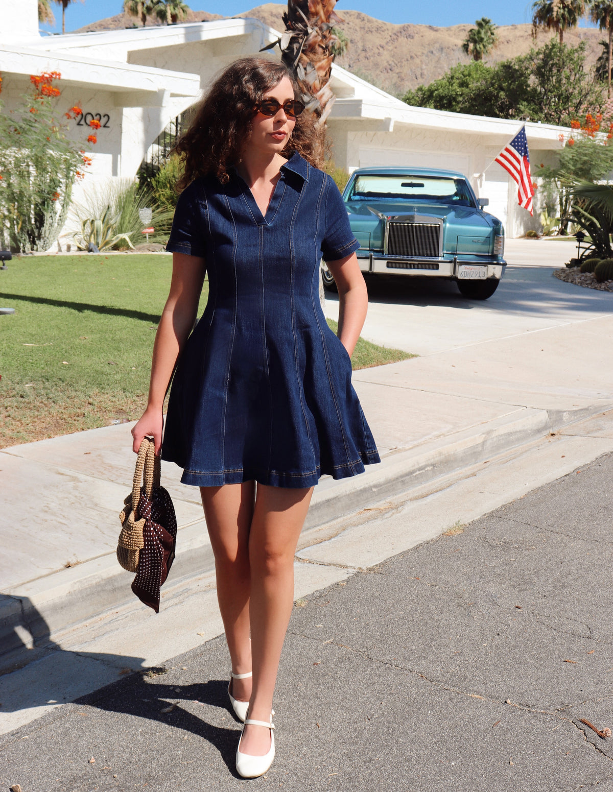 Woman in a blue dress walking on a street with a vintage car and house in the background