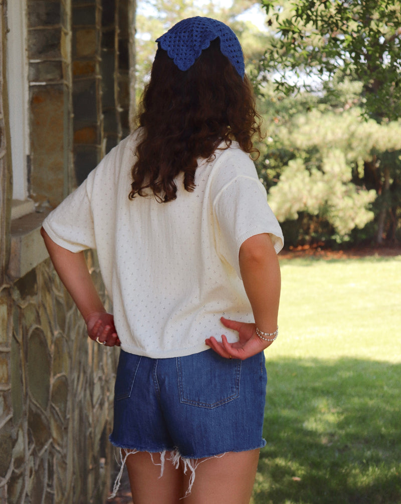 Person wearing a white top and blue shorts with a blue headscarf, standing outdoors.