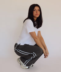 Person wearing dark gray pants with blue stripes and a white shirt against a plain background