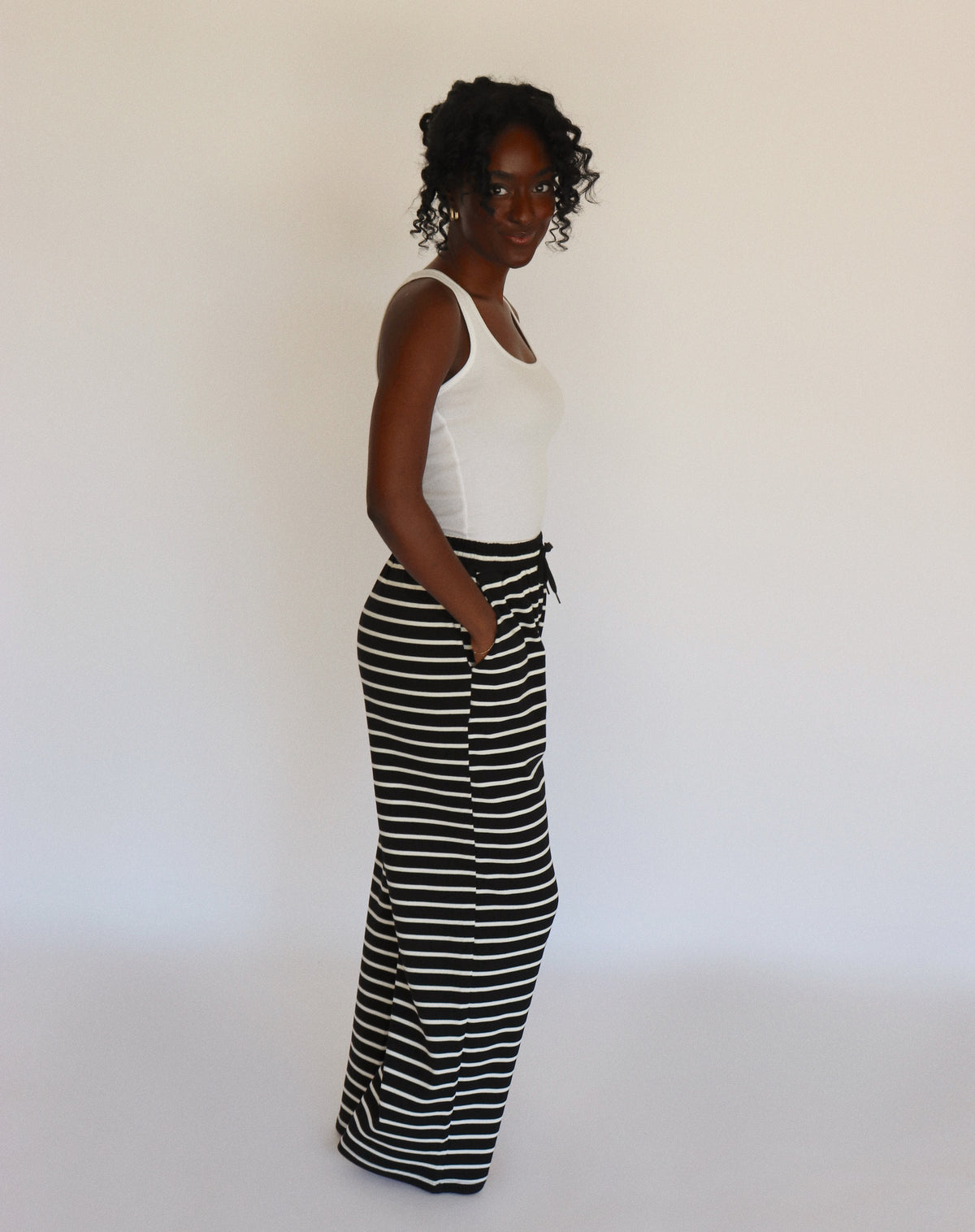 Woman wearing a white tank top and black and white striped pants on a white background