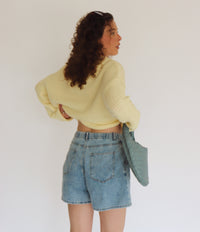 Person wearing a yellow sweater and denim shorts against a plain background