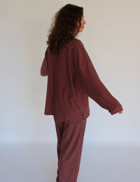 A woman modeling a matching two-piece loungewear set consisting of a long-sleeve top and pants, both featuring thin horizontal stripes in a pink and dark brown colorway.