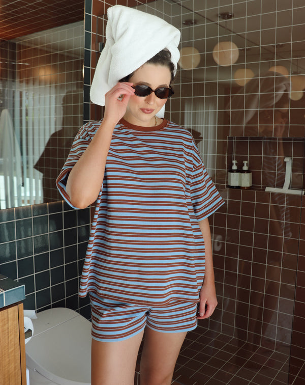 Person wearing a striped outfit with a towel on their head in a bathroom.