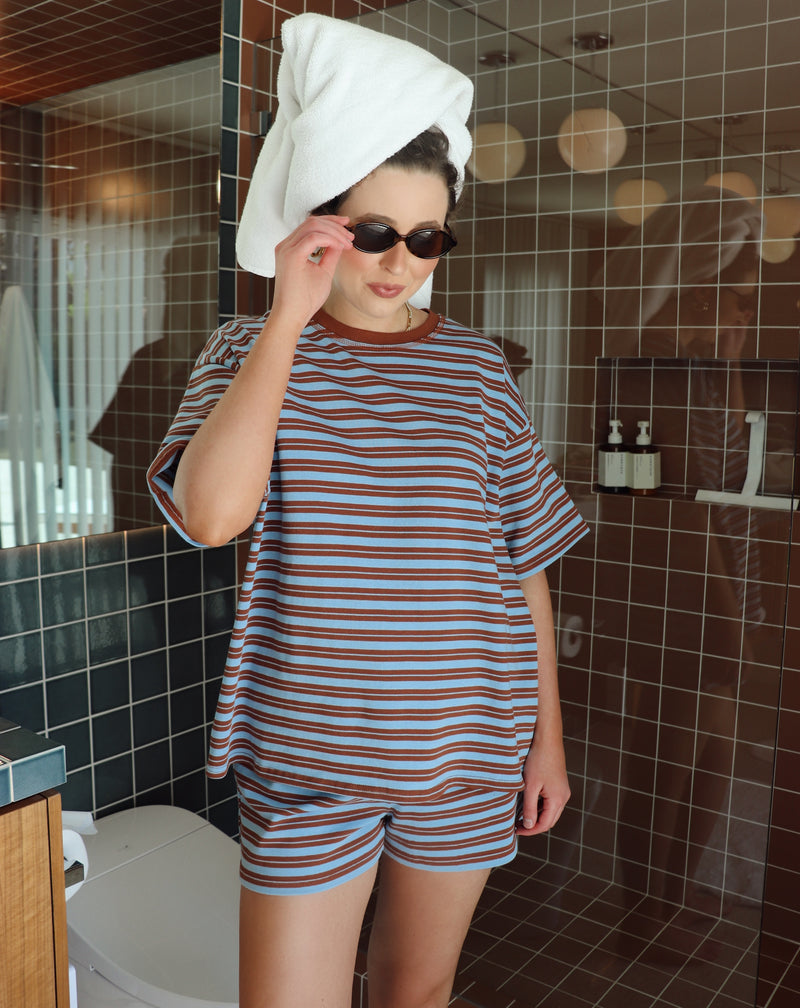 Person wearing a striped outfit with a towel on their head in a bathroom.