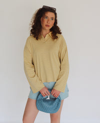 Woman wearing a yellow striped shirt and denim shorts holding a blue bag against a white background