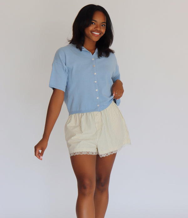 Woman wearing a blue short sleeve cardigan and cream shorts against a white background