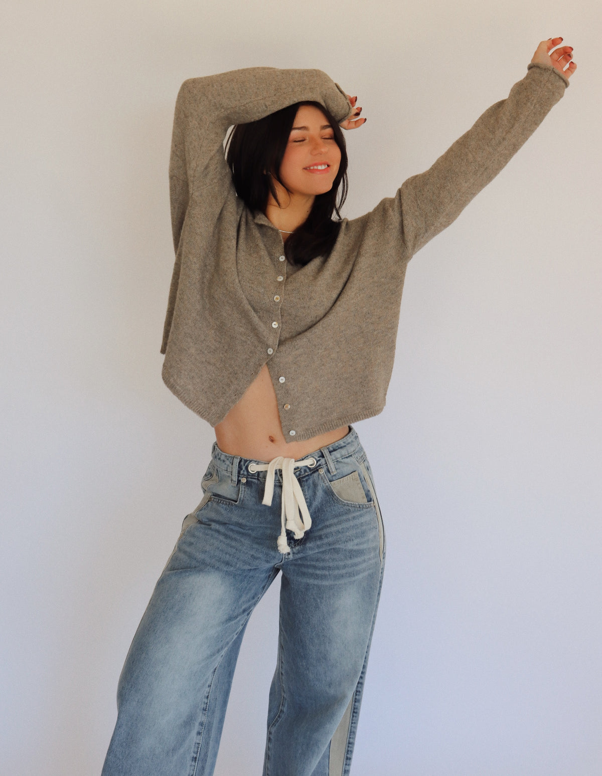 Woman wearing a taupe cardigan and blue jeans against a plain background