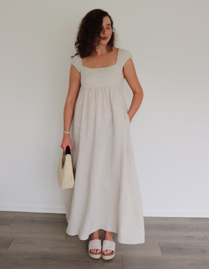 Woman wearing a long light-colored dress against a plain background