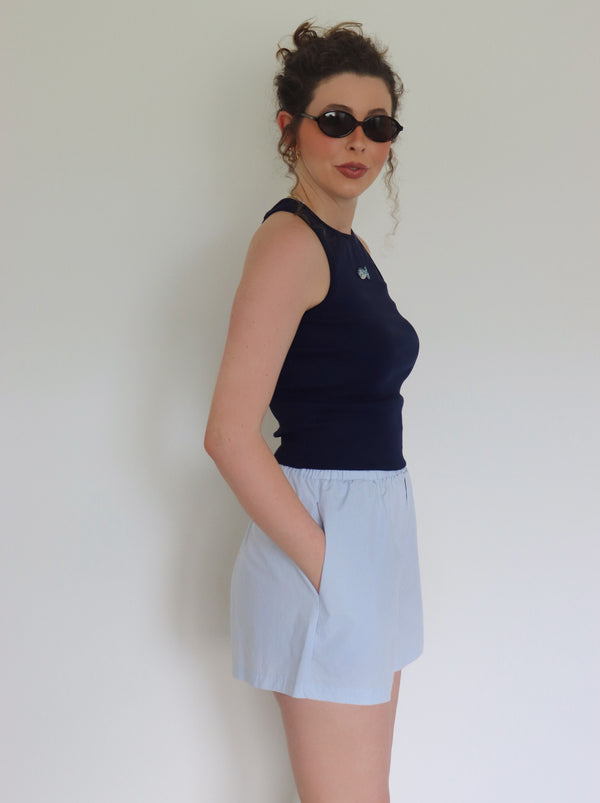 Woman wearing a navy top and light blue shorts against a plain background