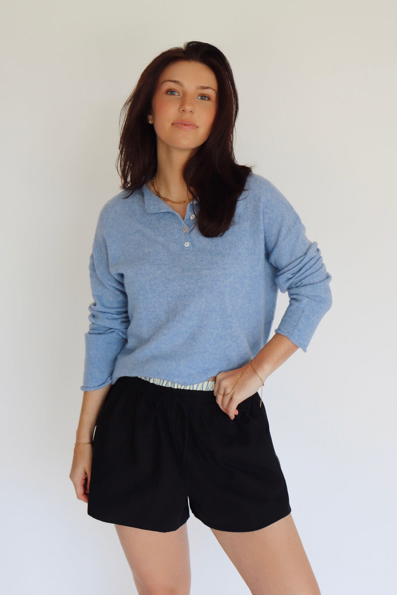 Woman wearing a blue long-sleeve shirt and dark navy shorts against a white background