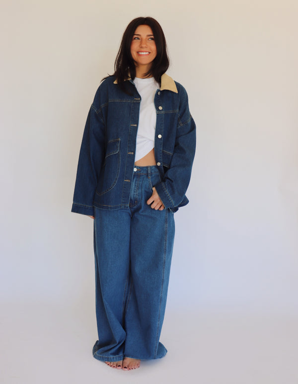 Person wearing a blue denim jacket and denim pants against a white background