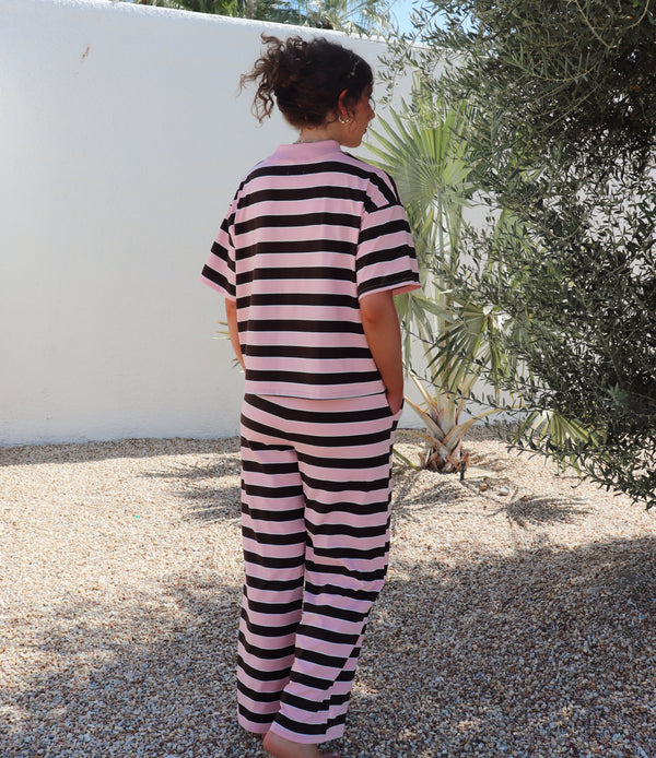Person wearing a brown and pink striped outfit standing outdoors with plants in the background