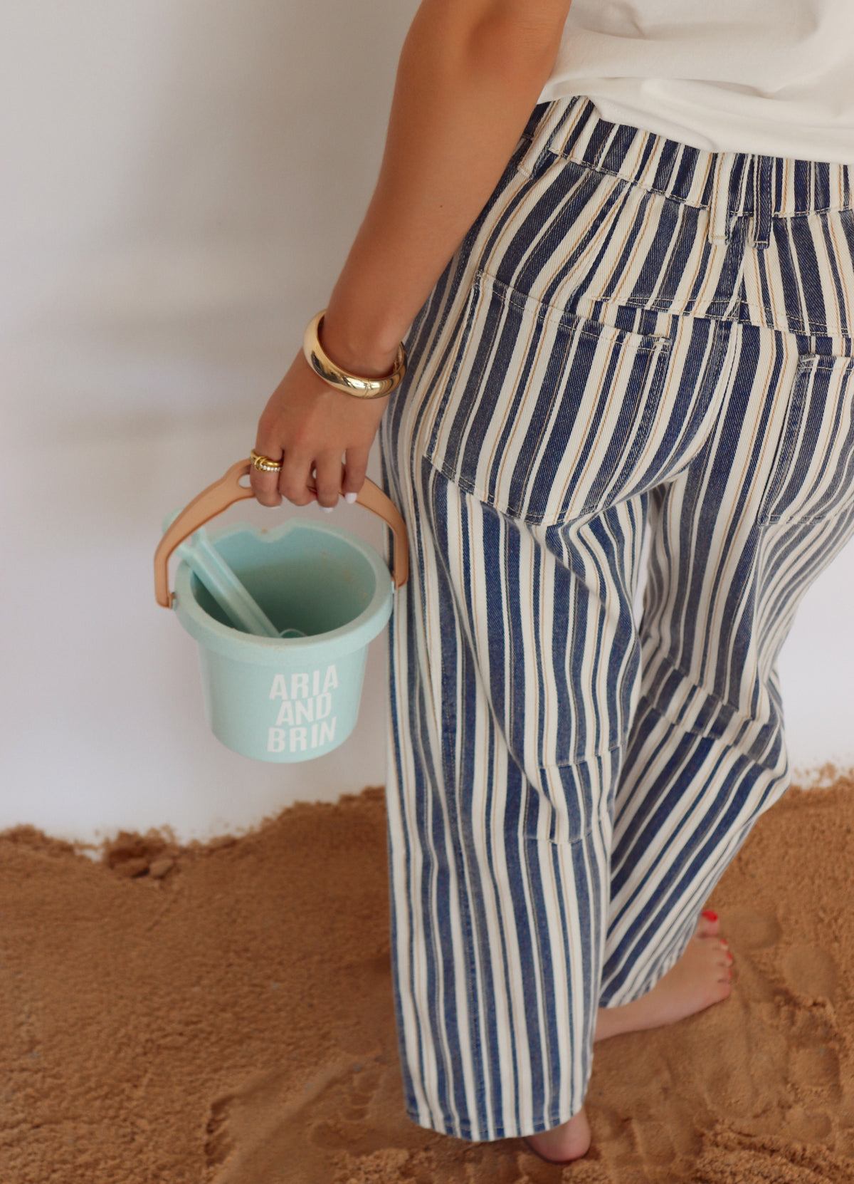 Person wearing blue and cream striped pants holding a bucket with sand