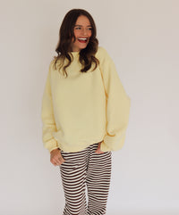 Woman wearing a light yellow pullover and striped pants against a plain background