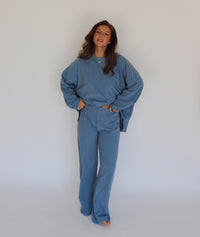 A woman modeling a matching blue striped lounge set, consisting of a long-sleeve top and wide-leg pants, against a plain white studio background.