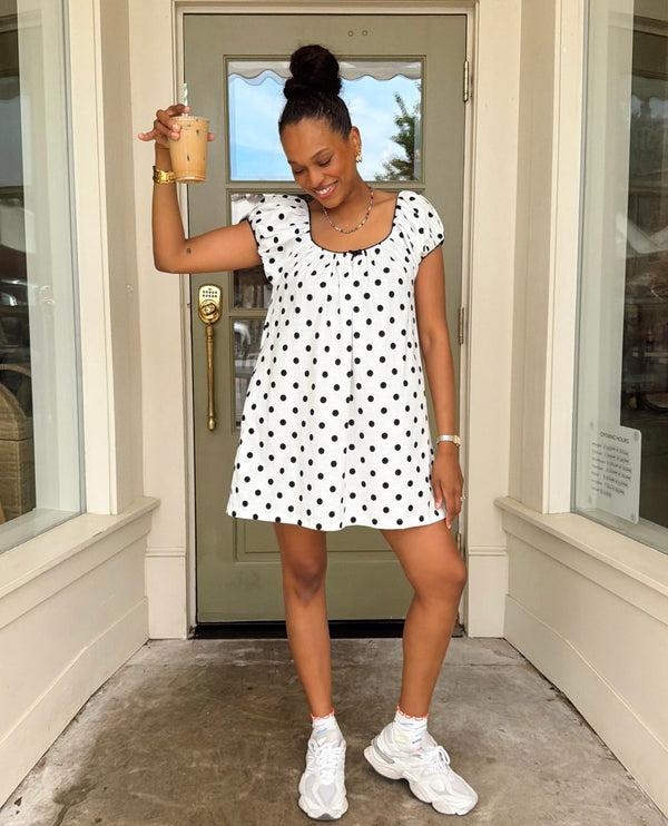 Woman in a polka dot dress standing in front of a door holding a drink.