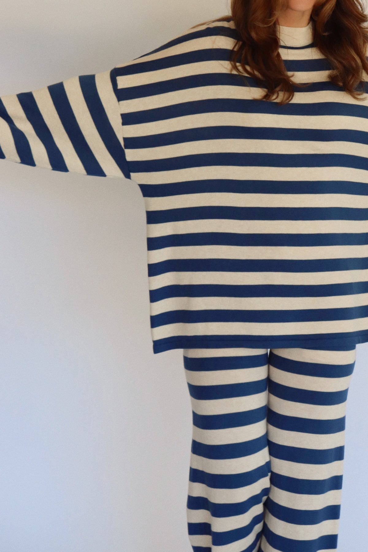 A woman wearing a matching two-piece loungewear set with blue and beige horizontal stripes, featuring a long-sleeve top and wide-leg pants, standing against a plain white background.