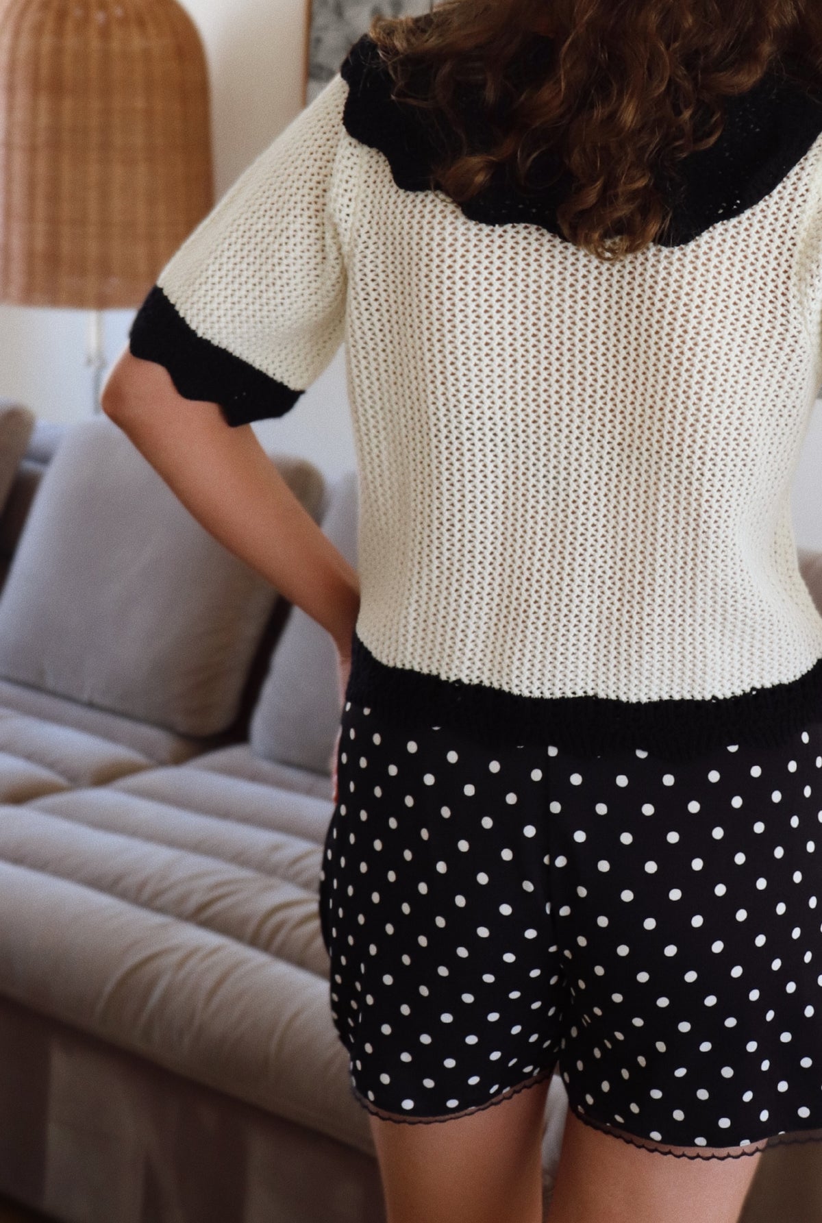 Woman wearing a black and white outfit with polka dot shorts in a living room.